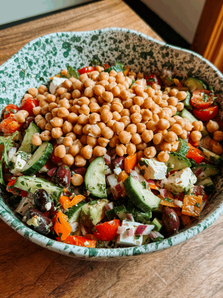 greek salad with avocado, feta, and chickpeas in a green speckled bowl