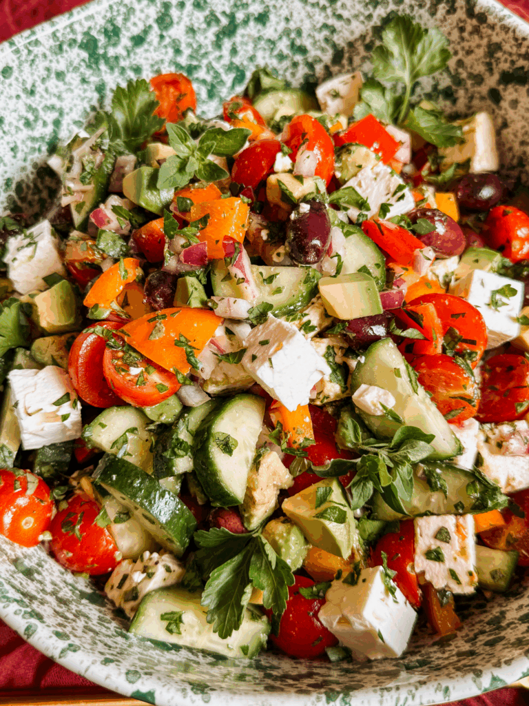 mediterranean greek salad with avocado, feta, cucumbers, peppers, tomatoes, and olives in a serving bowl