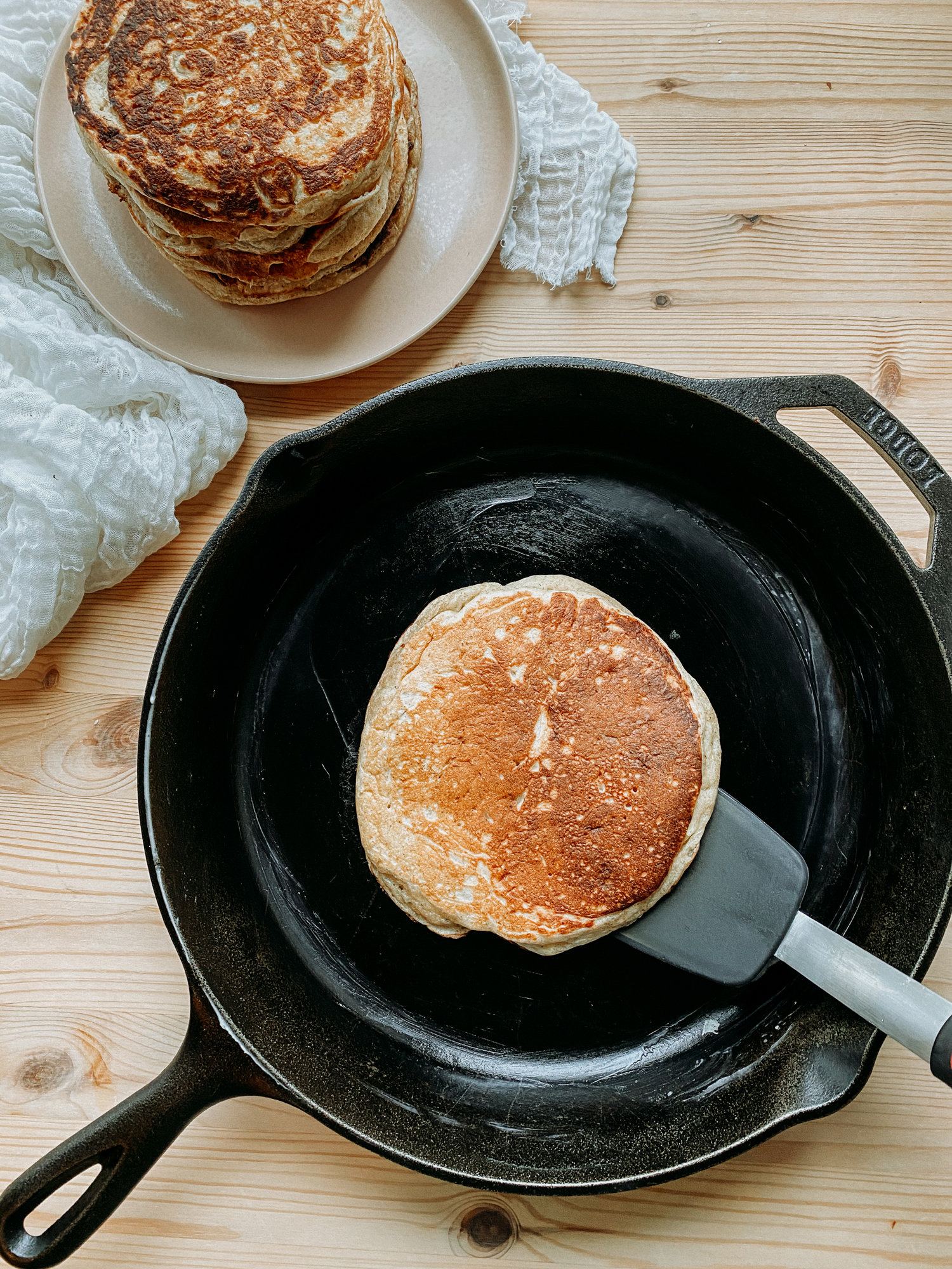 a silicone spatula flipping a pancake in a cast iron pan