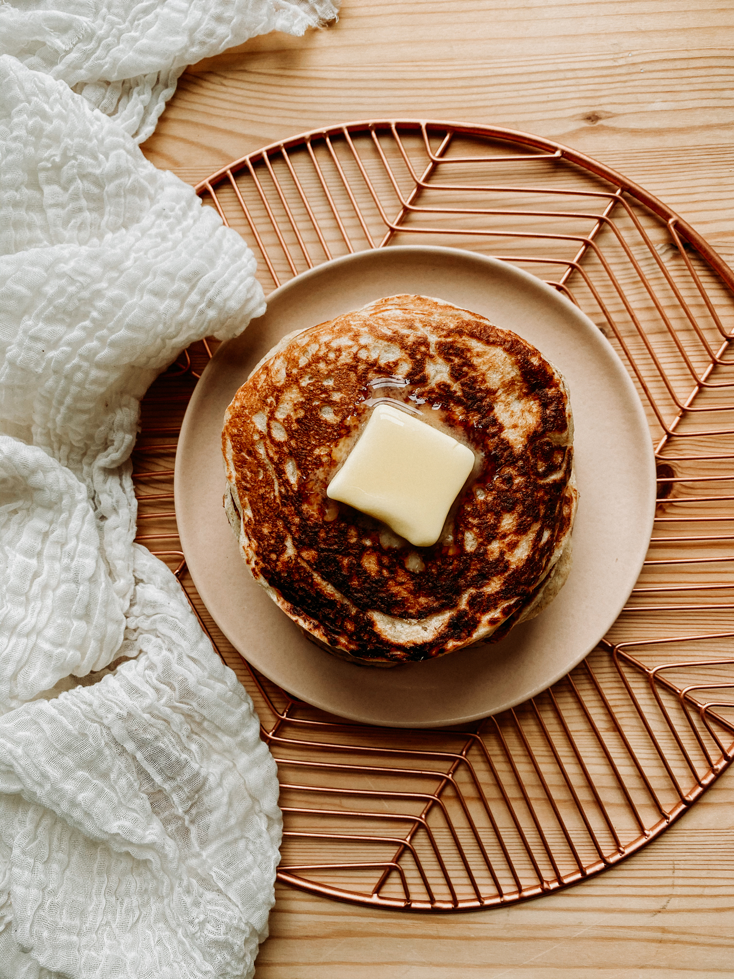 a pat of butter melting on top of a hot stack of pancakes on a peach colored plate
