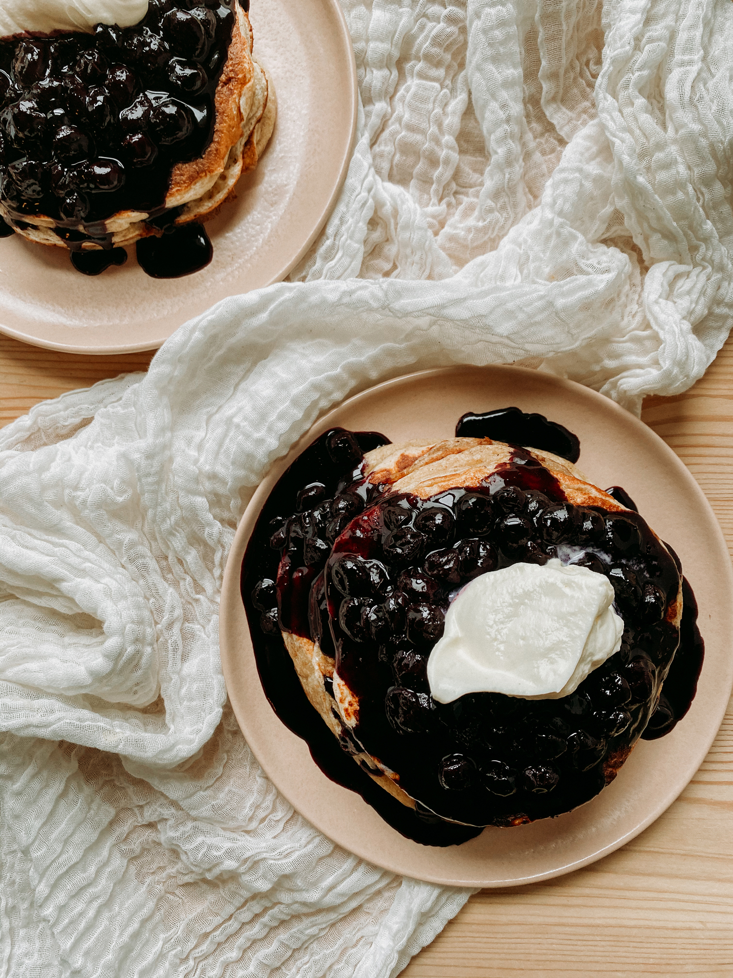 two pink plates with pancakes covered in blueberry sauce and whipped cream