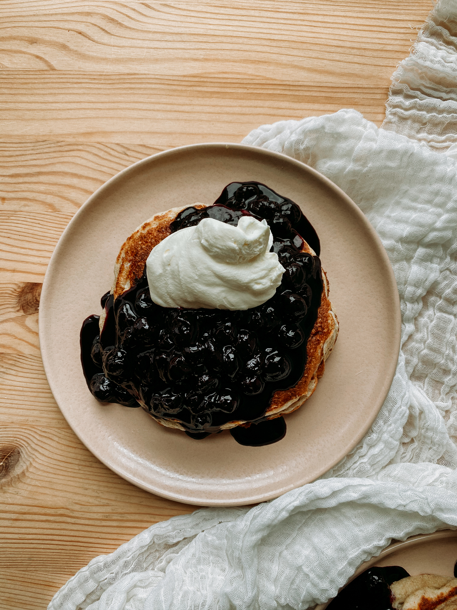 a pink plate with pancakes covered in blueberry sauce and whipped cream