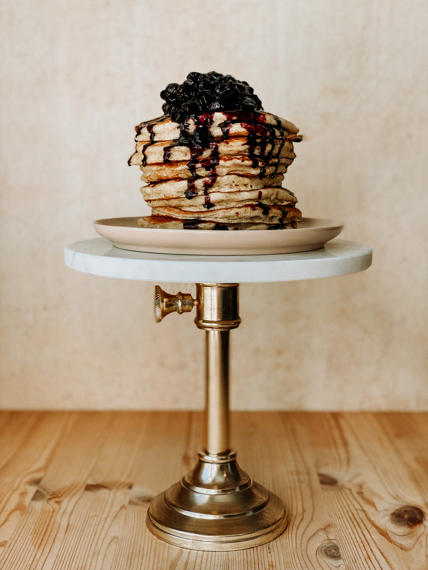 pancakes with blueberry sauce stacked on a pink plate on a cake stand