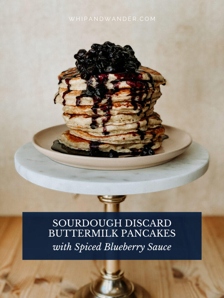 spiced blueberry sauce topped sourdough pancaked on a plate on a white and bronze stand