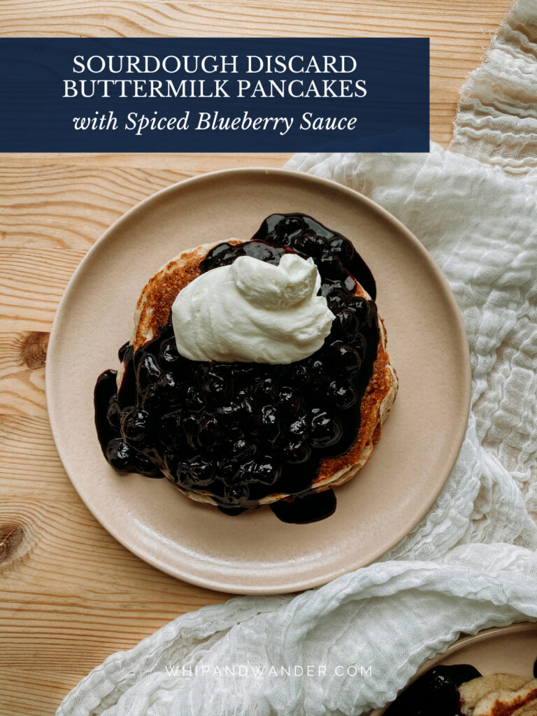 a pink plate with a whipped cream and blueberry sauce topped pancake