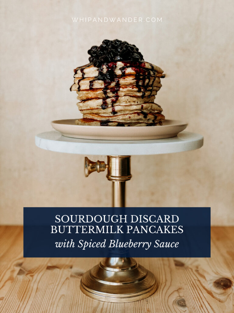 a stack of pancakes toped with spiced blueberry sauce resting on a pink plate on top of a cake stand