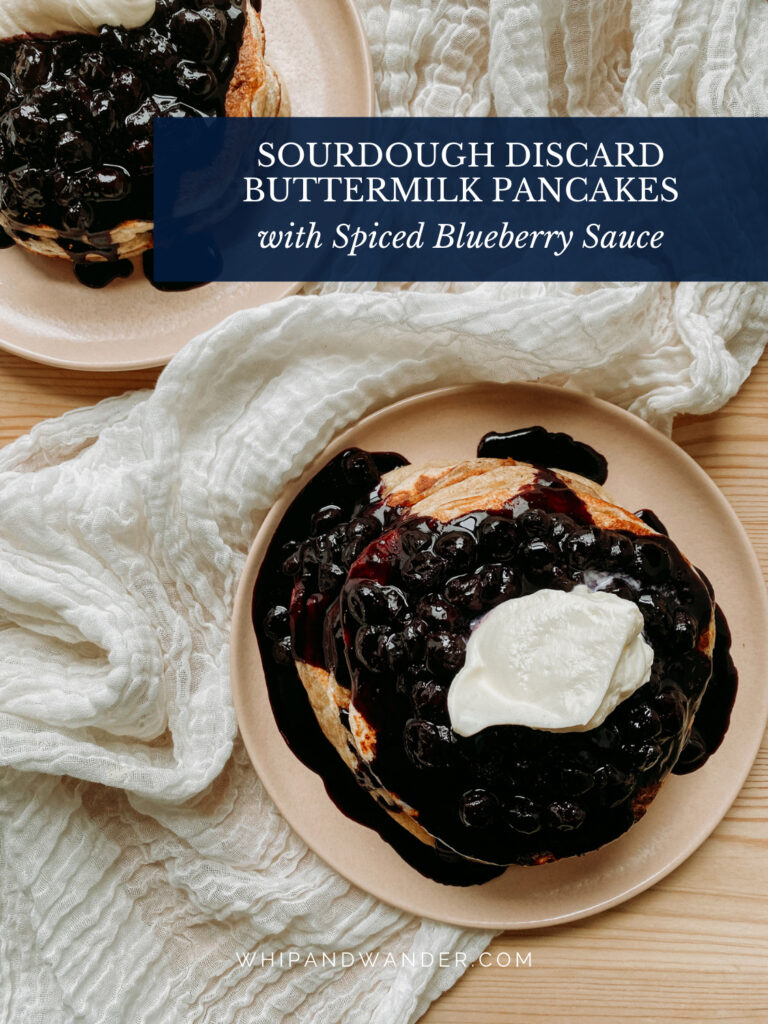two pink plates with pancakes covered in spiced blueberry sauce and whipped cream
