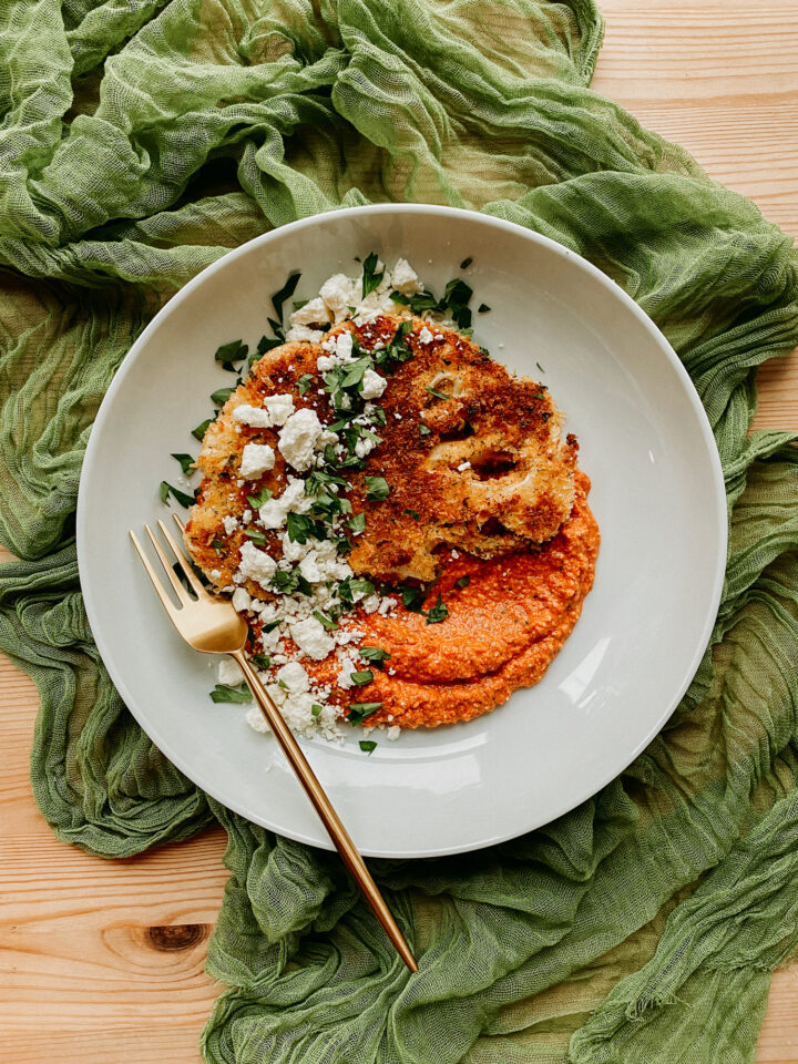 Crispy Cauliflower with Romesco and Feta in a large white bowl with a gold fork resting in the bowl and the plate on a green cloth