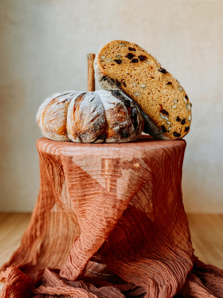 A loaf of Pumpkin Sourdough Bread cut in half and resting on a fabric lined cake stand