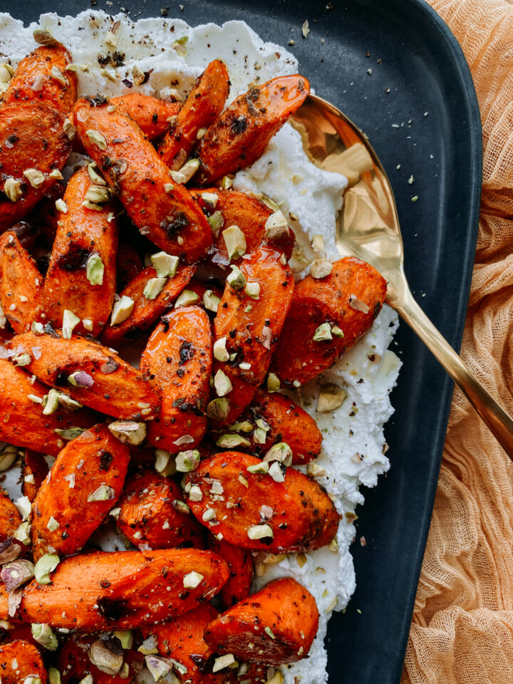a gold spoon resting in labneh cheese with roasted za'atar carrots on top