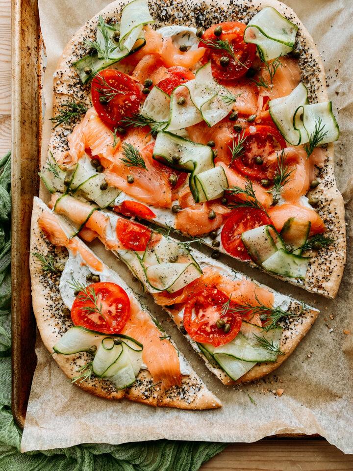 a bagel pizza with smoked salmon and cucumber partially cut into slices