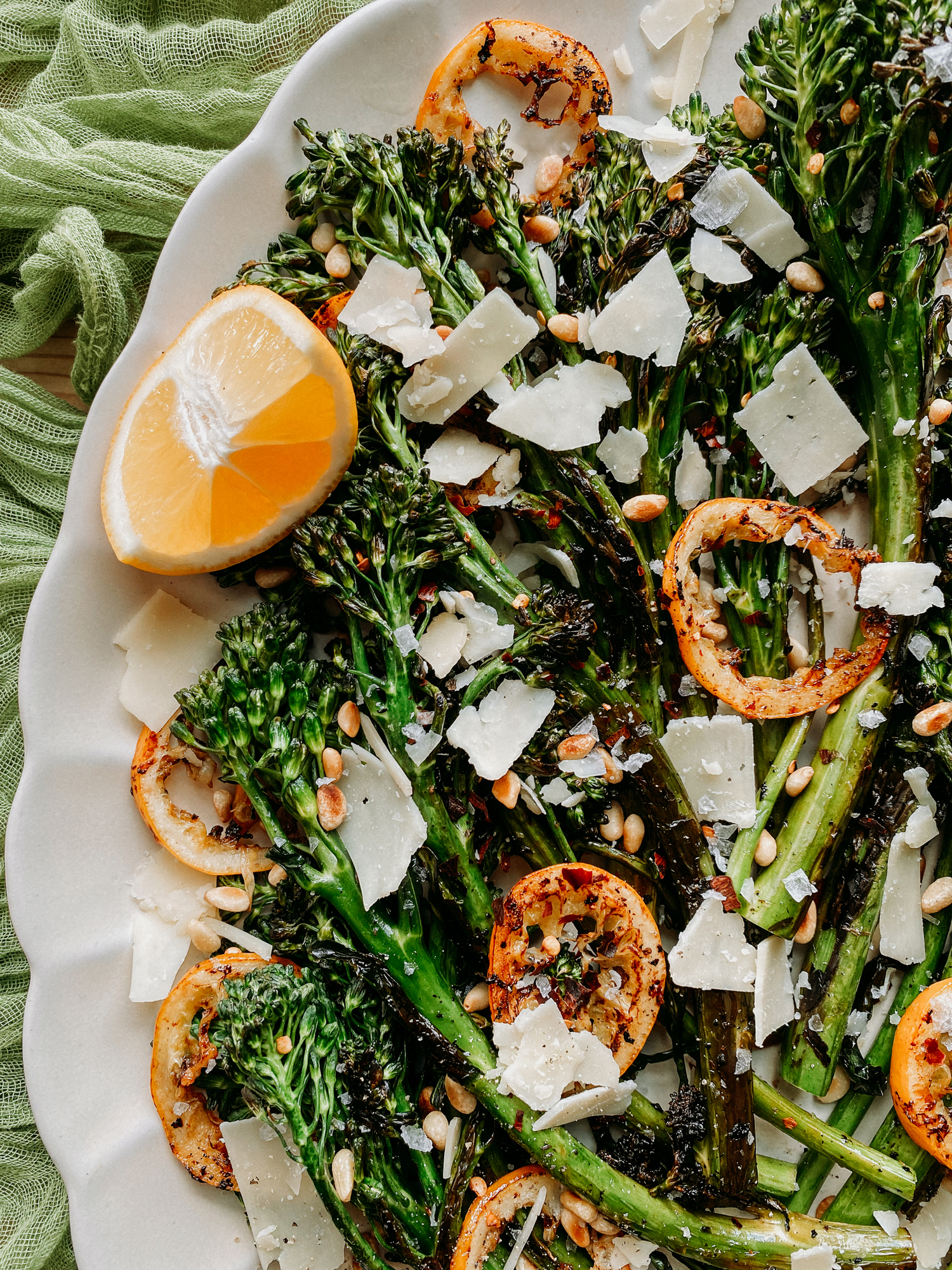 a wedge of lemon adorns a platter of pan cooked broccolini and lemon slices
