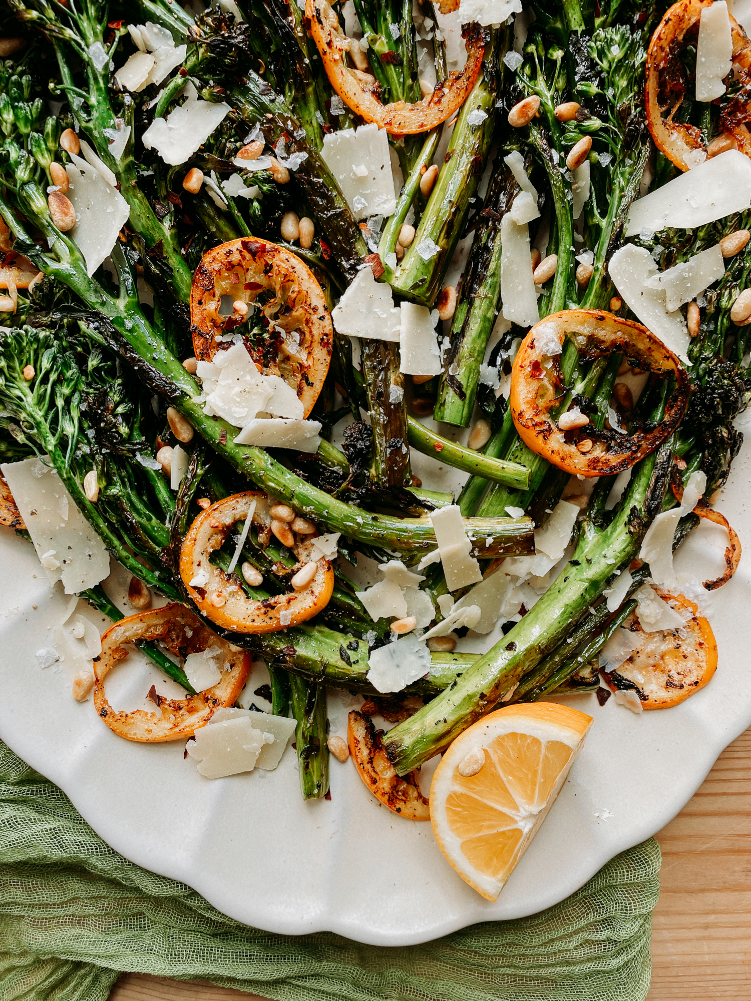 a white dish with broccolini, lemon, cheese, and nuts