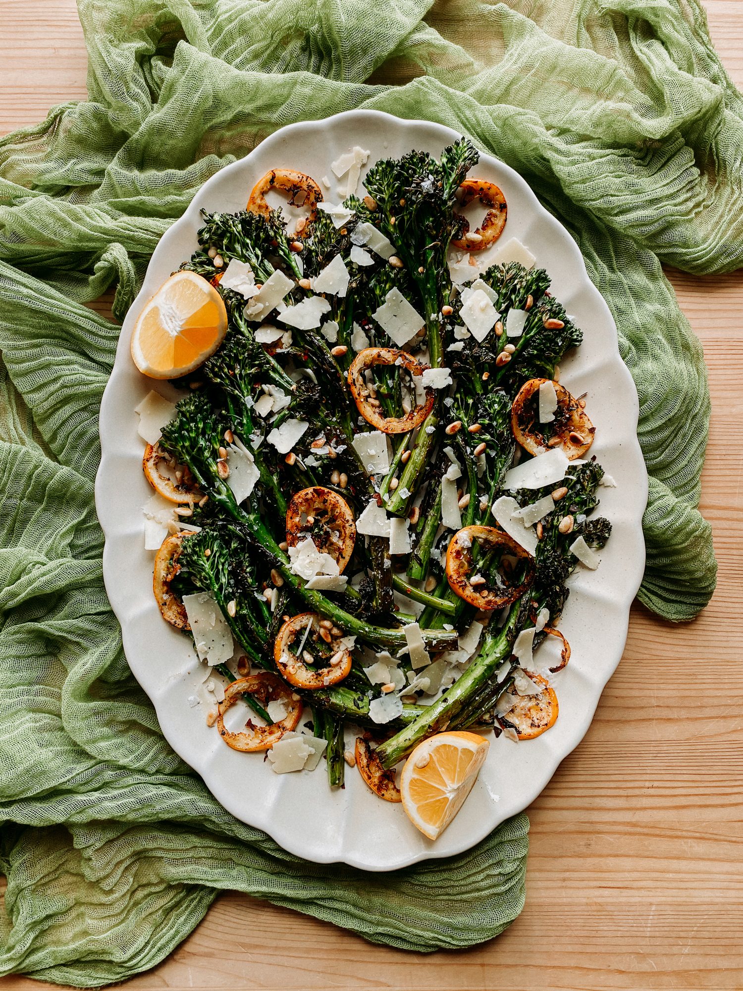 a platter with Charred Broccolini with Lemon, Pine Nuts, Parmesan , and browned lemon slices