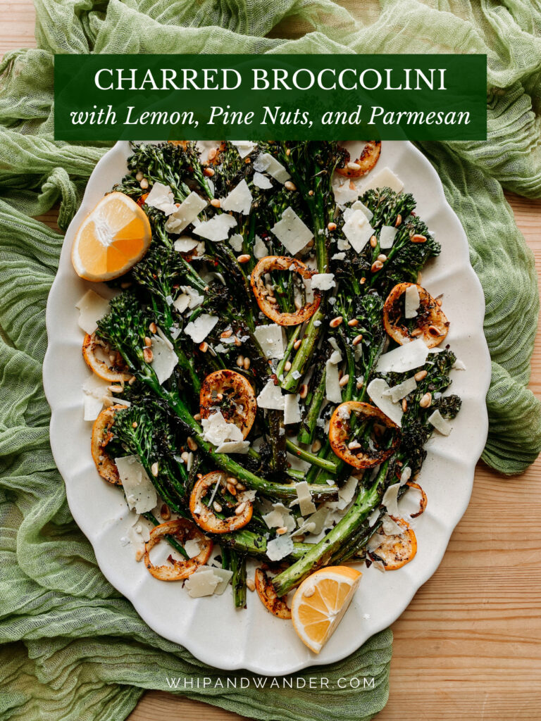 a pile of cooked broccolini and lemon on a white platter on a green cloth