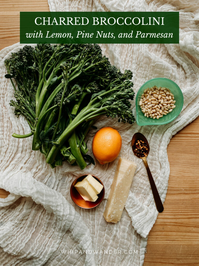 raw broccolini bundles with red pepper flakes, a lemon, butter, and pine nuts on a white gauzy cloth