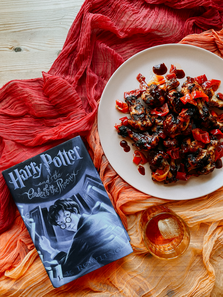 a harry potter book resting on gauzy red and orange cloth next to a plate of grilled chicken wings