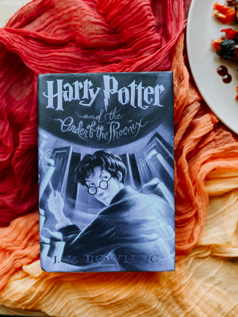 a harry potter book with a blue cover resting on orange and red gauzy cloths