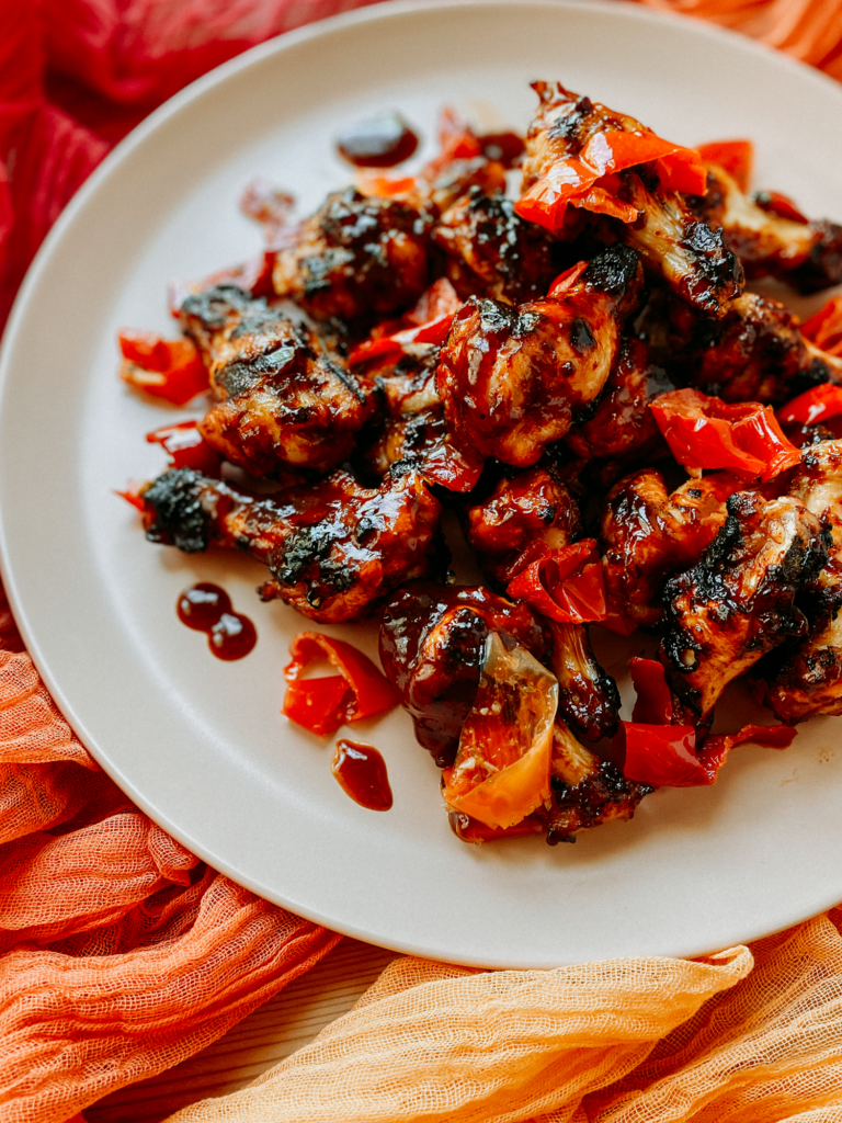 red pickled pepper topped bbq chicken wings on a light pink plate