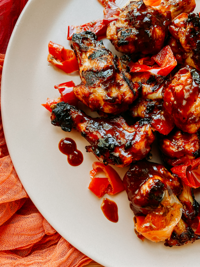 grilled chicken wings with bbq sauce and pickled red peppers on a light pink platter