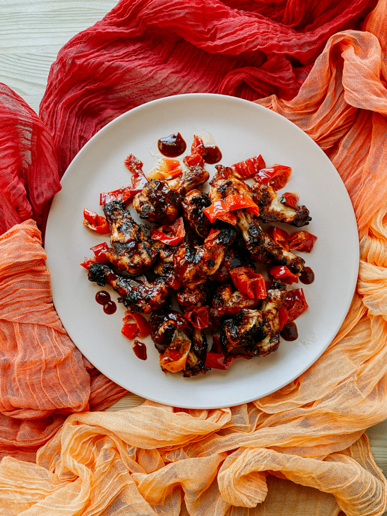 a light pink platter topped with grilled bbq chicken wings resting on red and orange gauzy cloths
