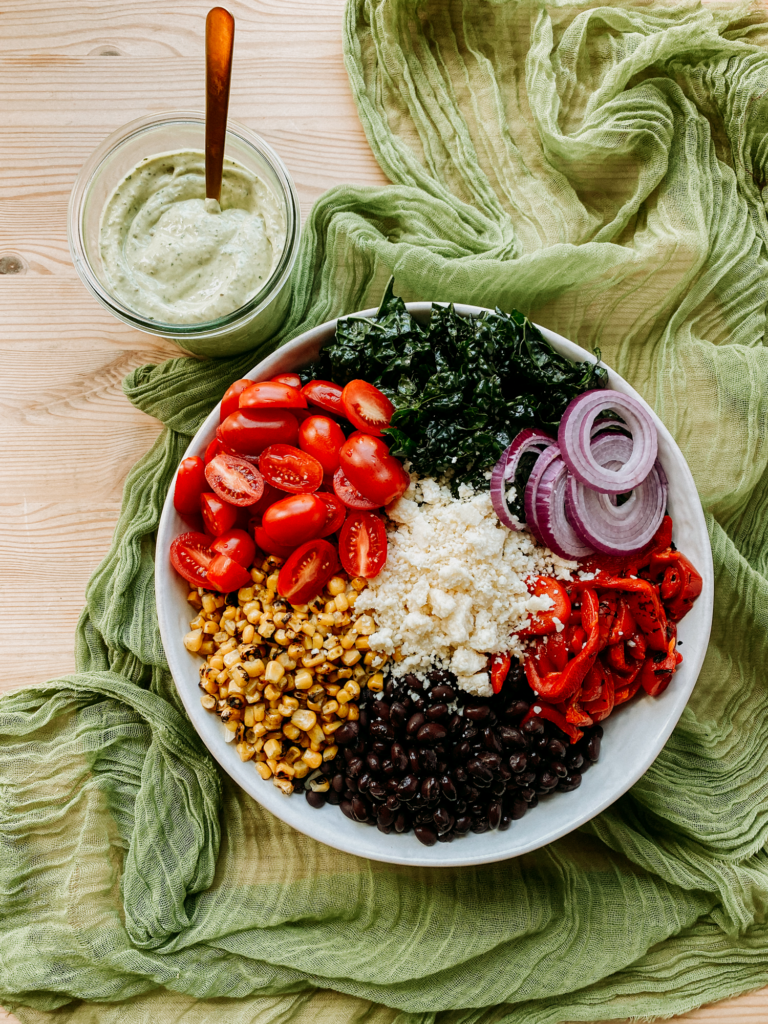 a bowl filled with veggies, kale, and beans, and a jar of avocado lime ranch next to it