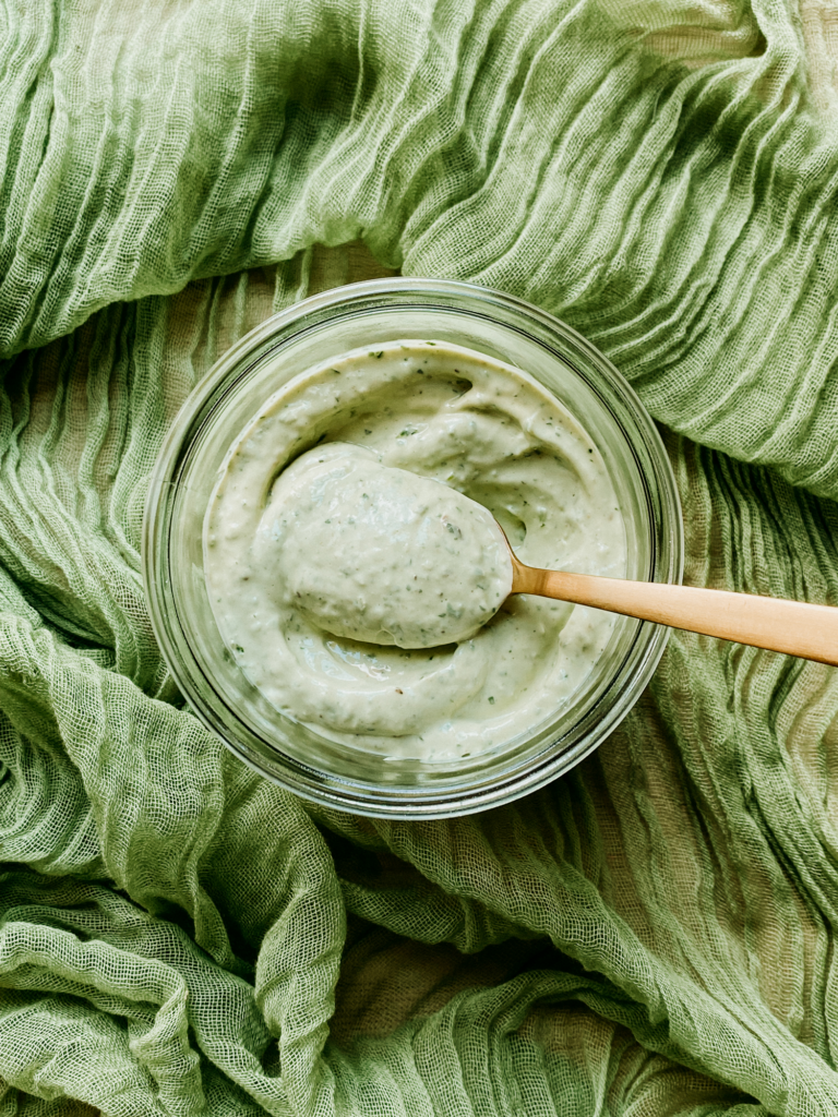 a gold spoon resting in a jar of avocado lime ranch on a gauzy green cloth