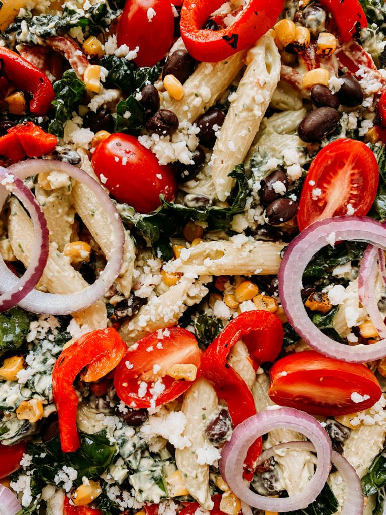 a pasta salad with tomatoes, red onion, cotija, black beans, corn, and kale