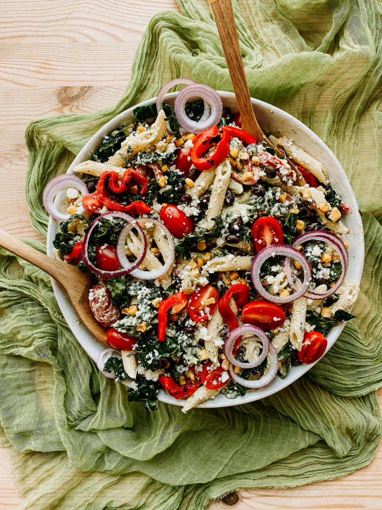 two wooden serving utensils resting in a large bowl with Southwest Pasta Salad on a green cloth