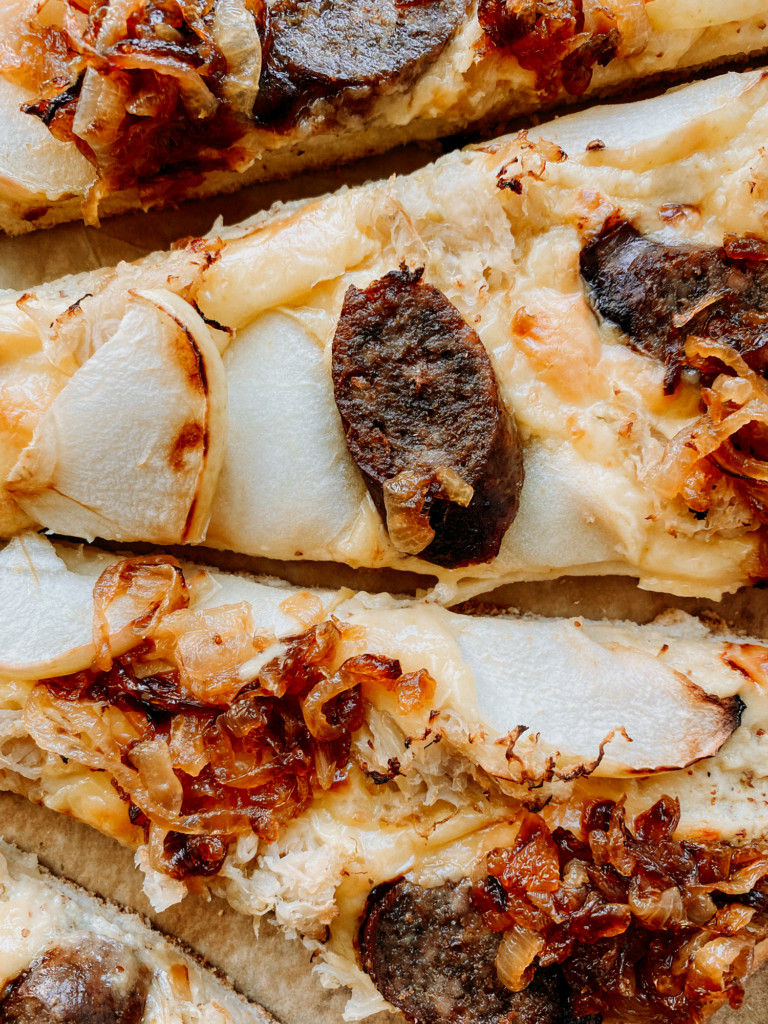 sliced bratwurst, apples, caramelized onion, and sauerkraut on top of pizza slices