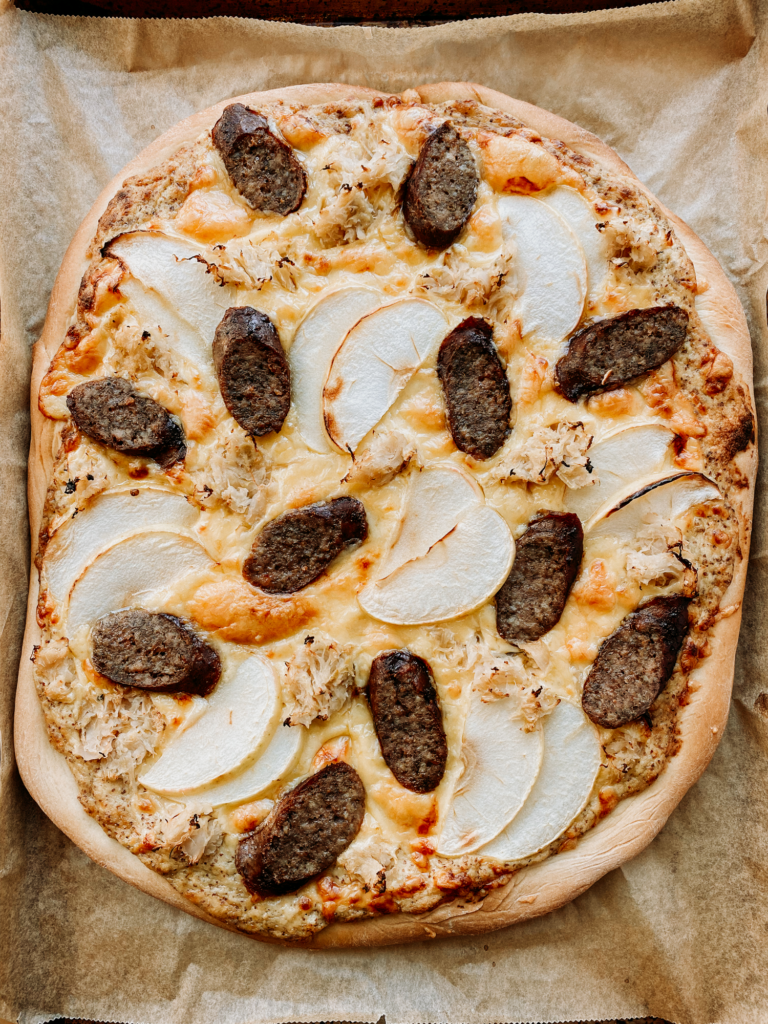 a pizza with bratwurst, gouda, and apple