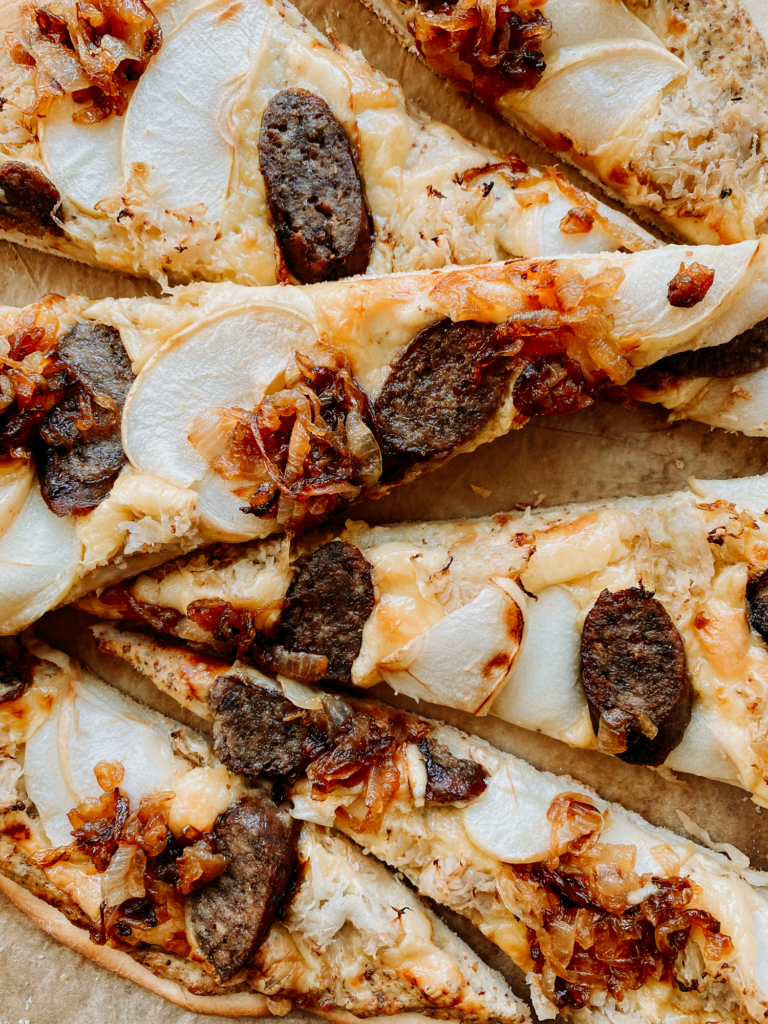 slices of pizza with gouda, bratwurst, sauerkraut, onion, and apples