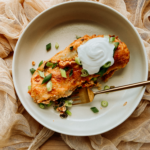 an enchilada in a shallow bowl with a gold fork