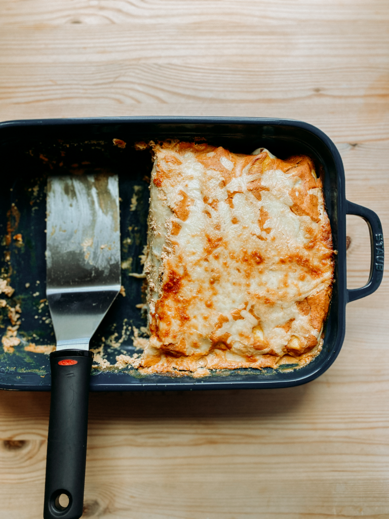 a half of a pan of enchiladas with a metal serving utensil resting in the dish