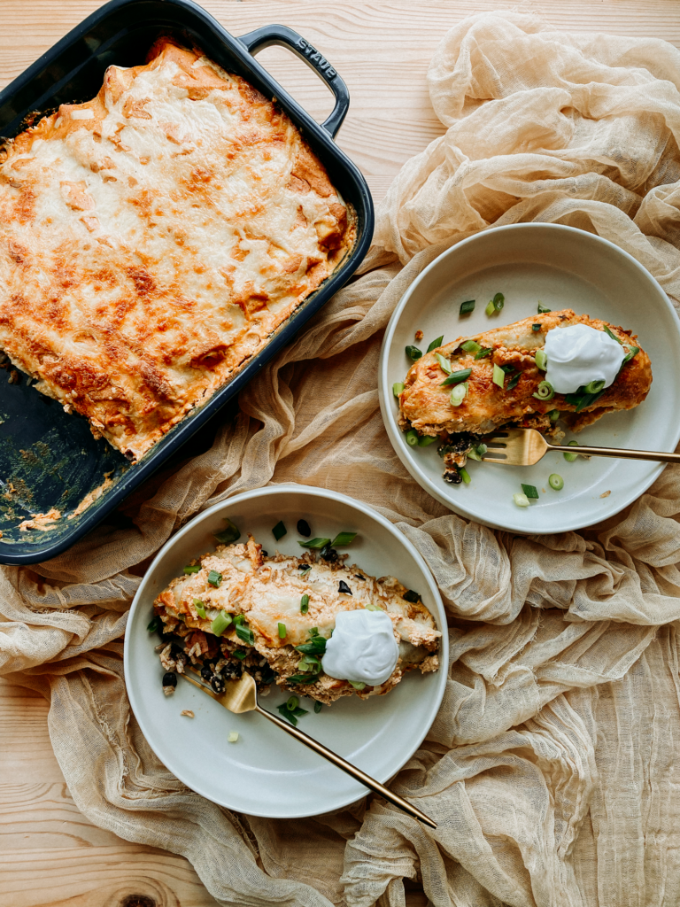 a tray of enchiladas next to two bowls containing an enchilada each