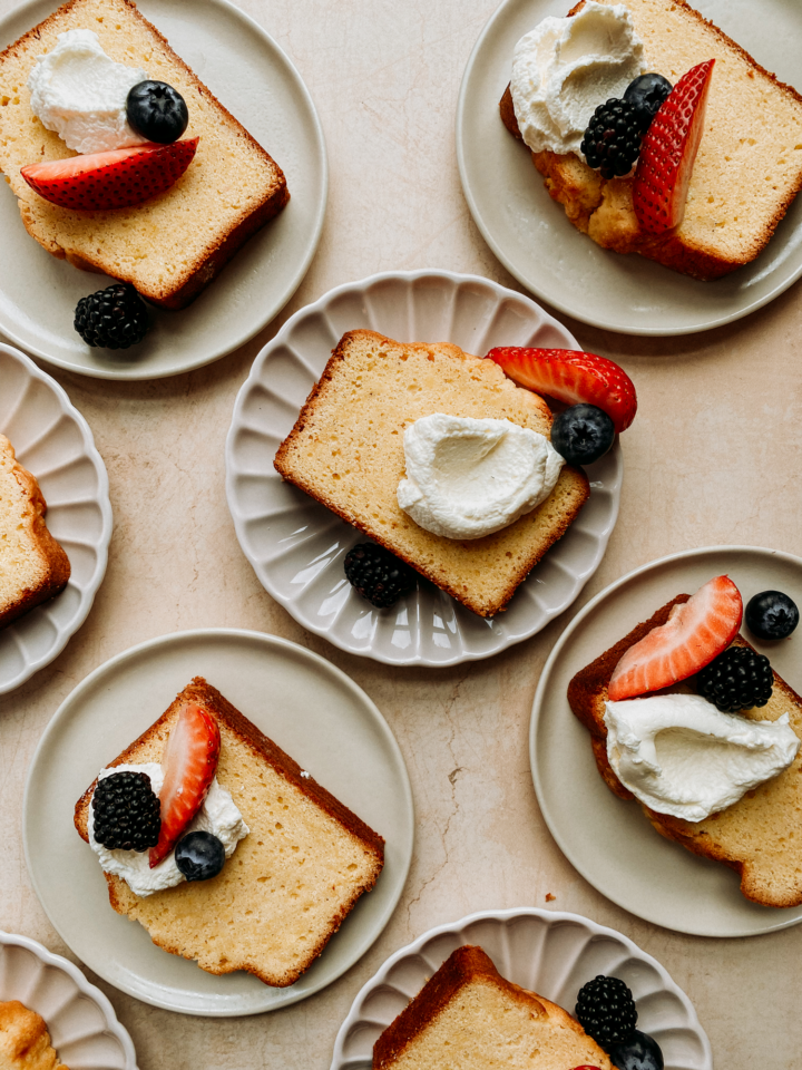 several plates with slices of pound cake, topped with whipped cream and berries on a neutral back ground