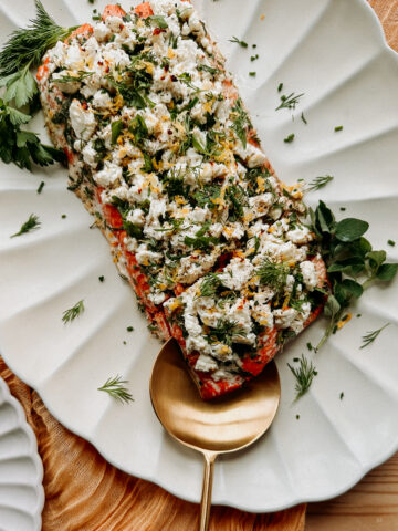 a gold spoon scooping up roasted salmon topped with fresh herbs and feta