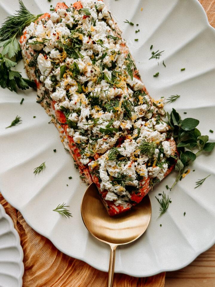 a gold spoon scooping up roasted salmon topped with fresh herbs and feta