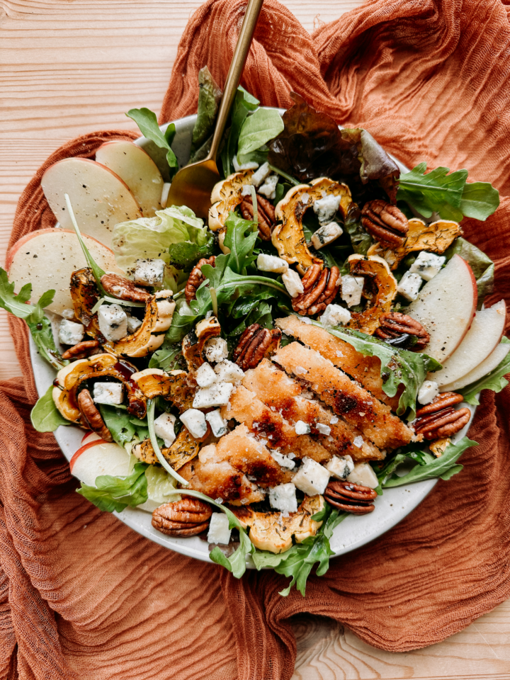 A leafy green salad in a bowl with apples, chicken, blue cheese, and squash