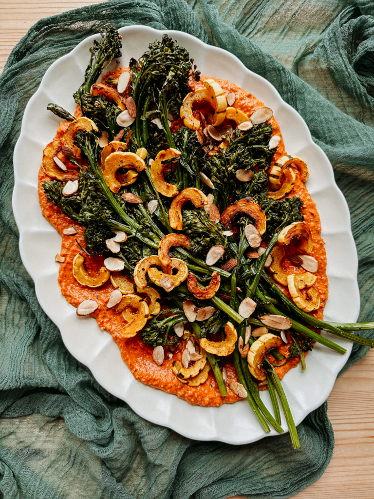a white platter topped with delicata squash, broccolini, almonds, and a bed of romesco sauce