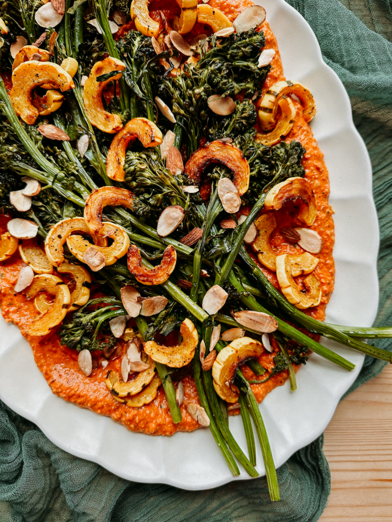 almonds, broccolini, squash, and red romesco sauce on a white platter