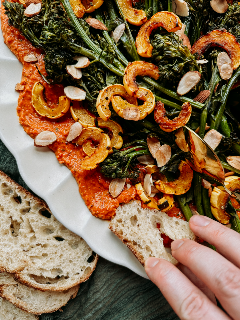 a hand using crusty bread to scoop up romesco with veggies