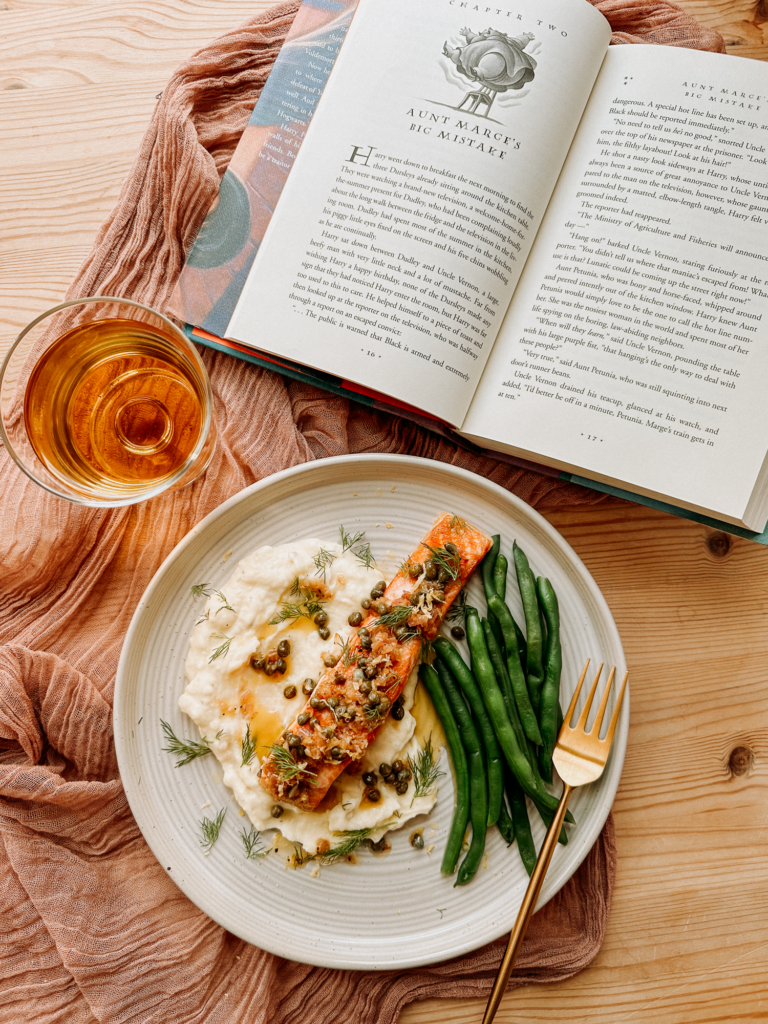 a plate of salmon, green beans, and pommes puree next to an open harry potter book