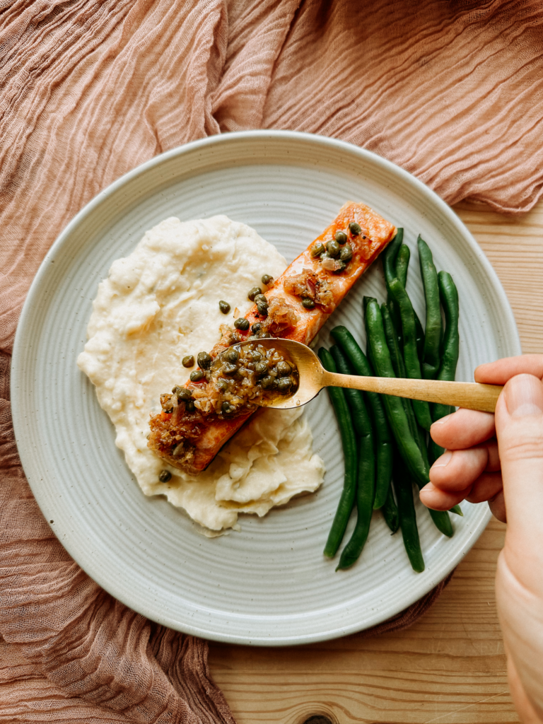 a gold spoon pouring caper butter sauce over salmon