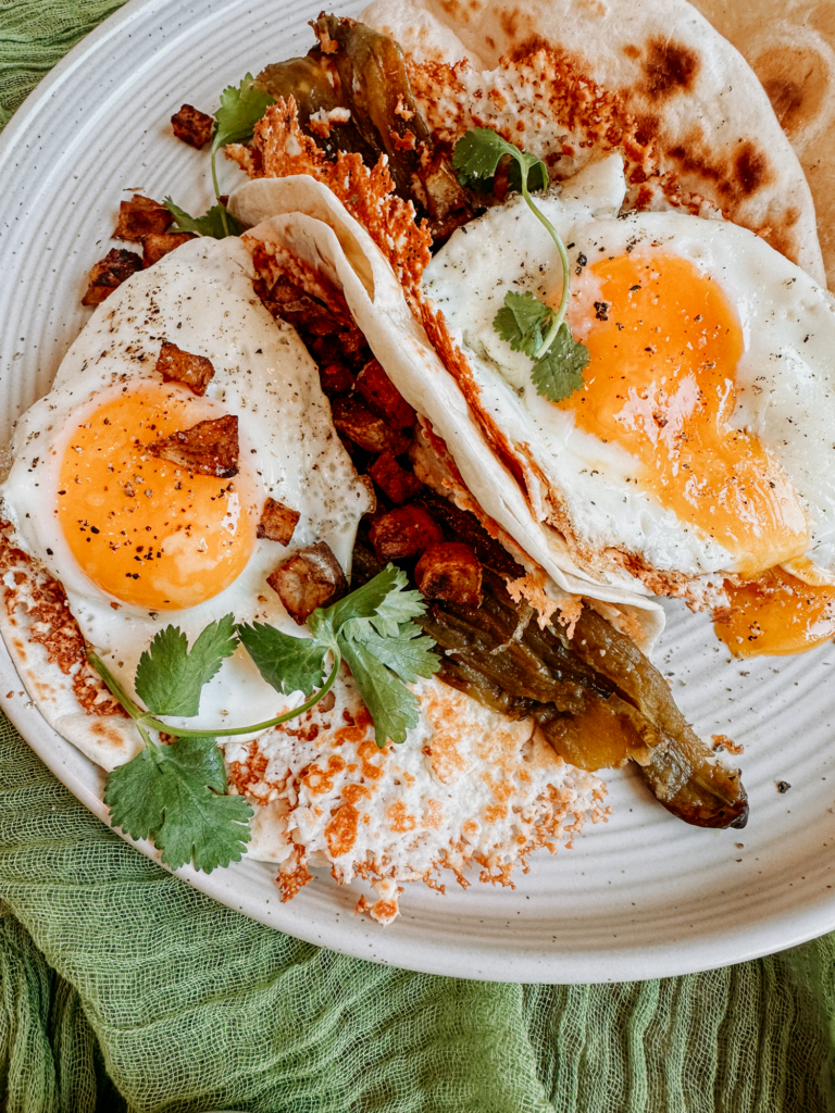 runny eggs, green chilis, and potatoes in flour tortillas on a white plate