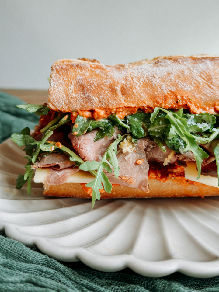 a closeup of a baguette with romesco sauce, arugula, and roast beef peeking out