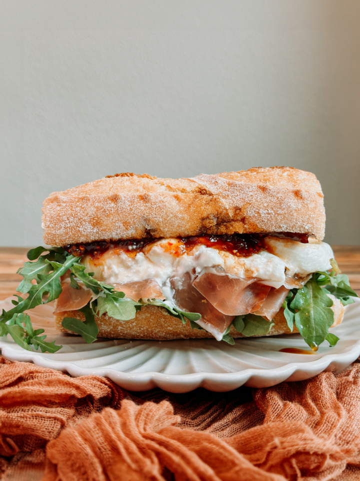a Prosciutto and Cheese Sandwich with Chili Fig Jam resting n a white plate on an orange cloth