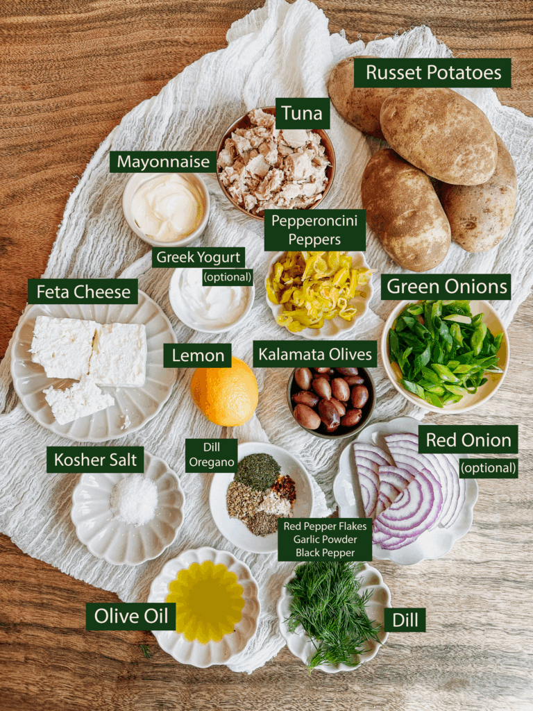 Labeled ingredient spread for Greek tuna salad baked potatoes, including tuna, feta, olives, lemon, herbs, and russet potatoes.