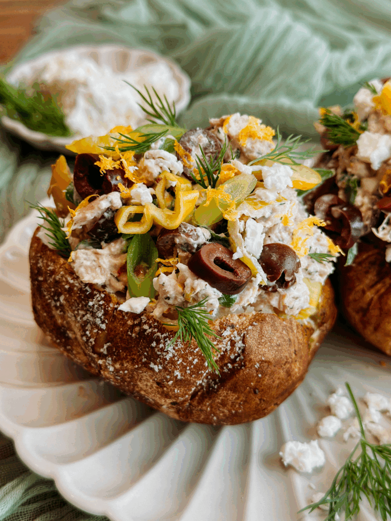 Top-down close-up of Greek tuna salad baked potato with olives, dill, lemon zest, and crumbled feta.
