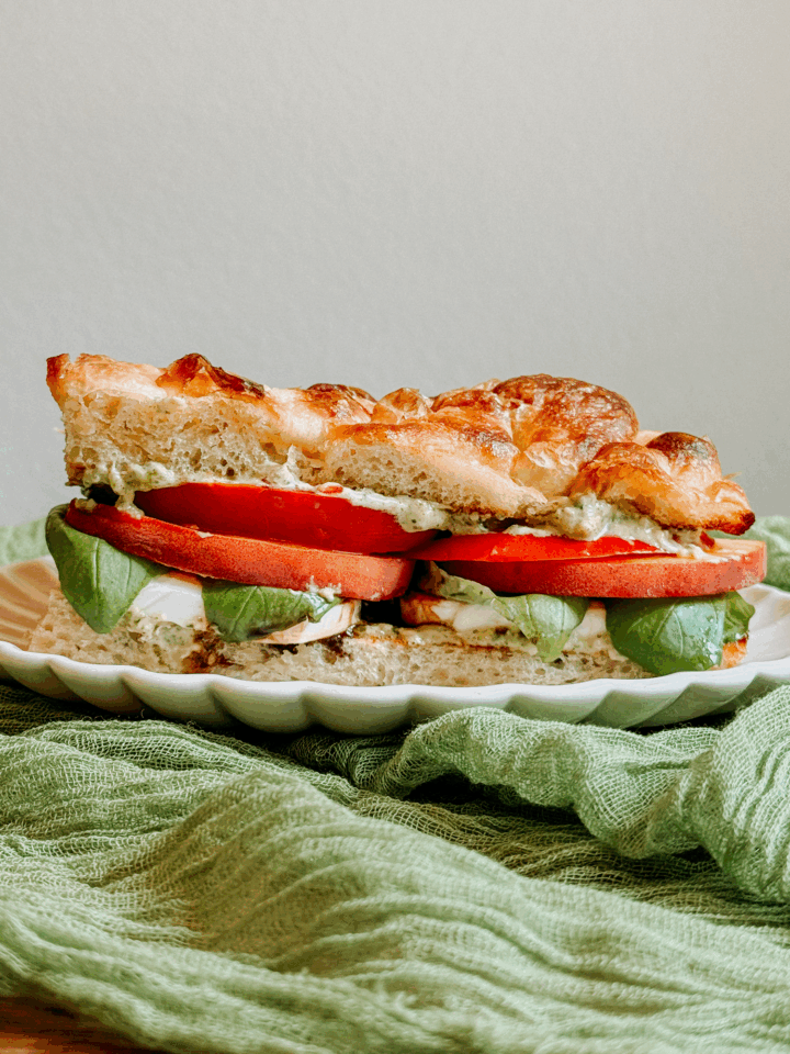 Side view of a peach caprese sandwich layered with fresh tomato, basil, mozzarella, and pesto mayo on toasted focaccia